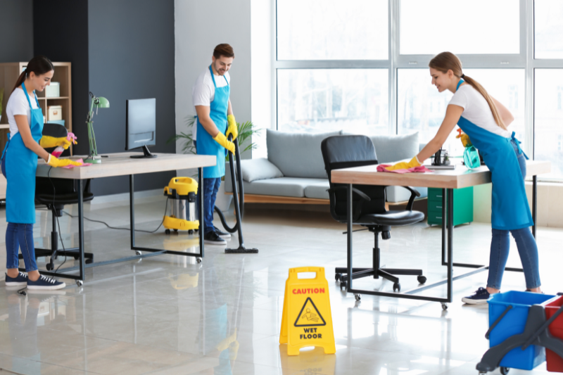 Three people cleaning a modern office space with blue aprons and gloves