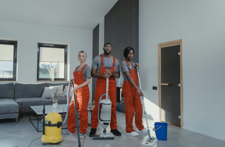 Three people in orange jumpsuits standing in a living room with cleaning equipment