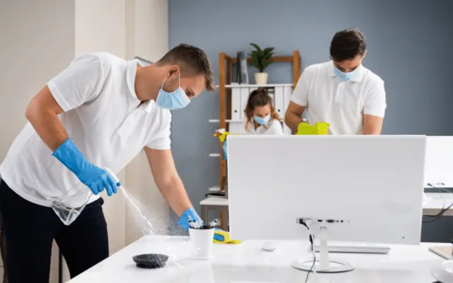 Two people performing quality home cleaning on a desk in an office setting.